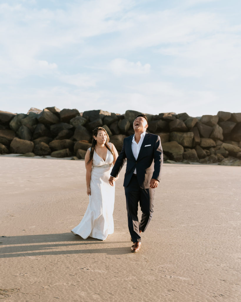 A bride and groom laughing while walking on the beach at Mission Beach in San Diego during their elopement.