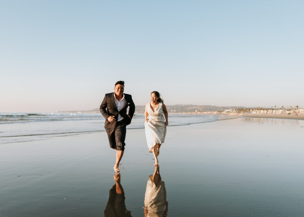 A bride and groom running during their elopement at Mission Beach in San Diego.