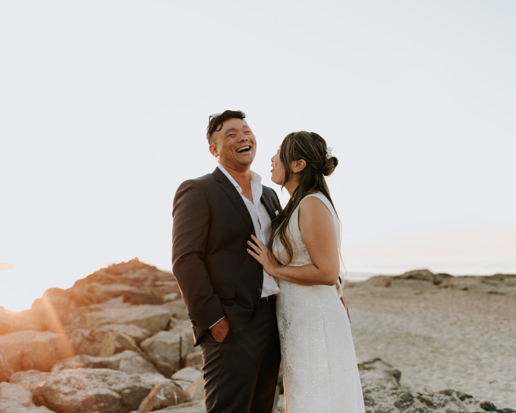 A bride and groom laughing during their elopement at Mission Beach in San Diego.