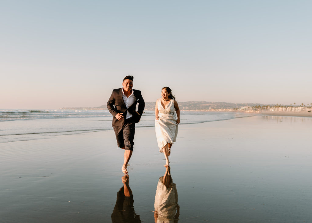 A photograph of a bride and groom running during their elopement in San Diego at Mission Bay.