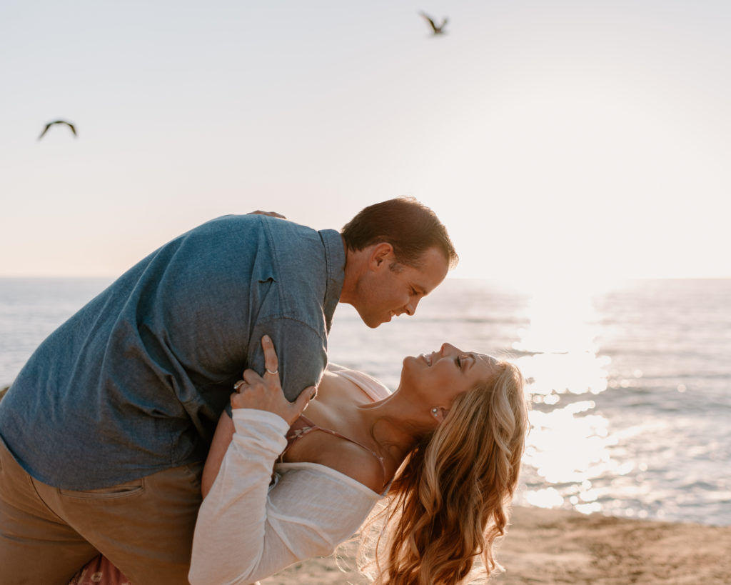 A photograph of a man and woman kissing near the ocean during their engagement session at Sunset Cliffs in San Diego, CA.