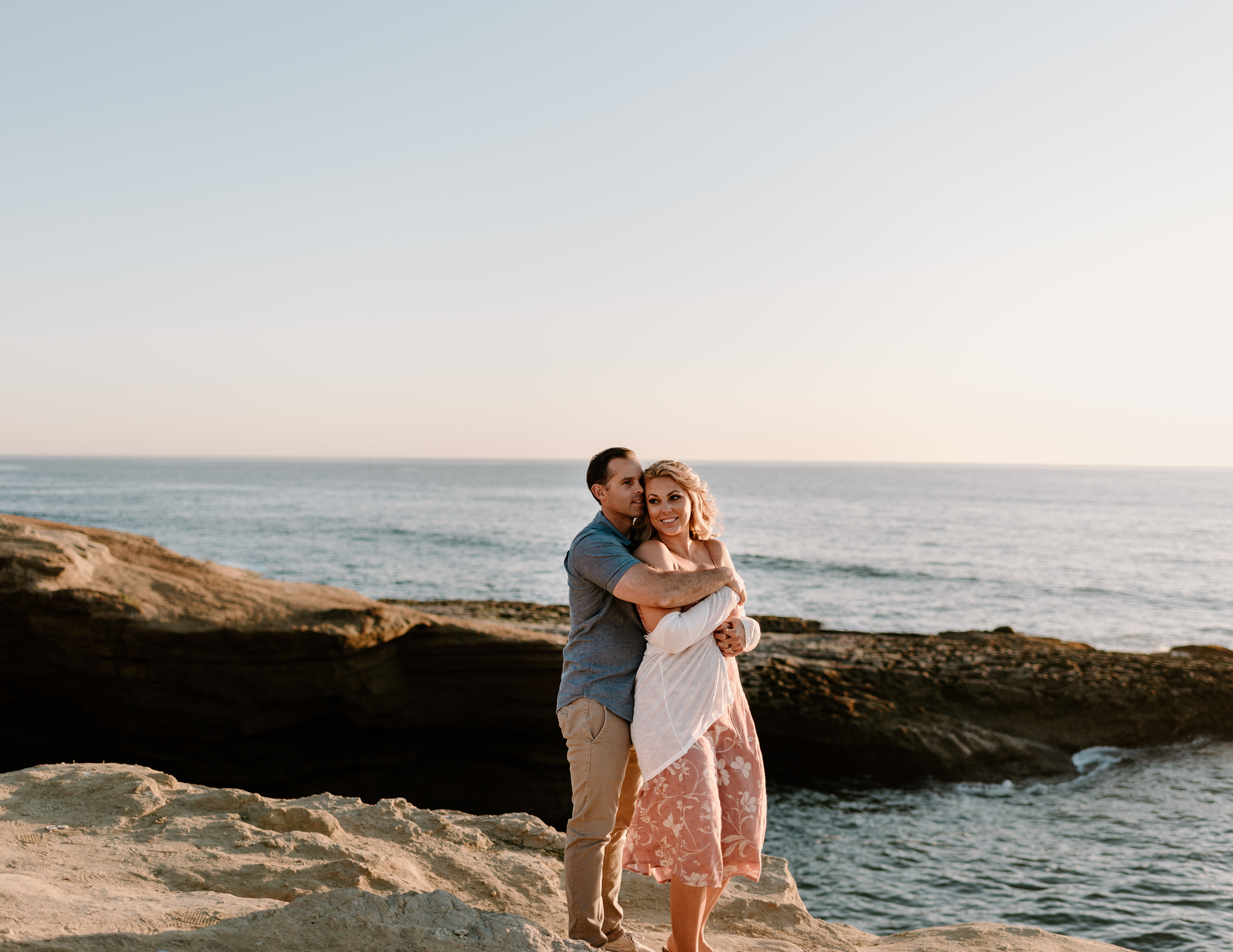 A photograph of a man and woman standing by the ocean at Sunset Cliffs during their engagement photo session.