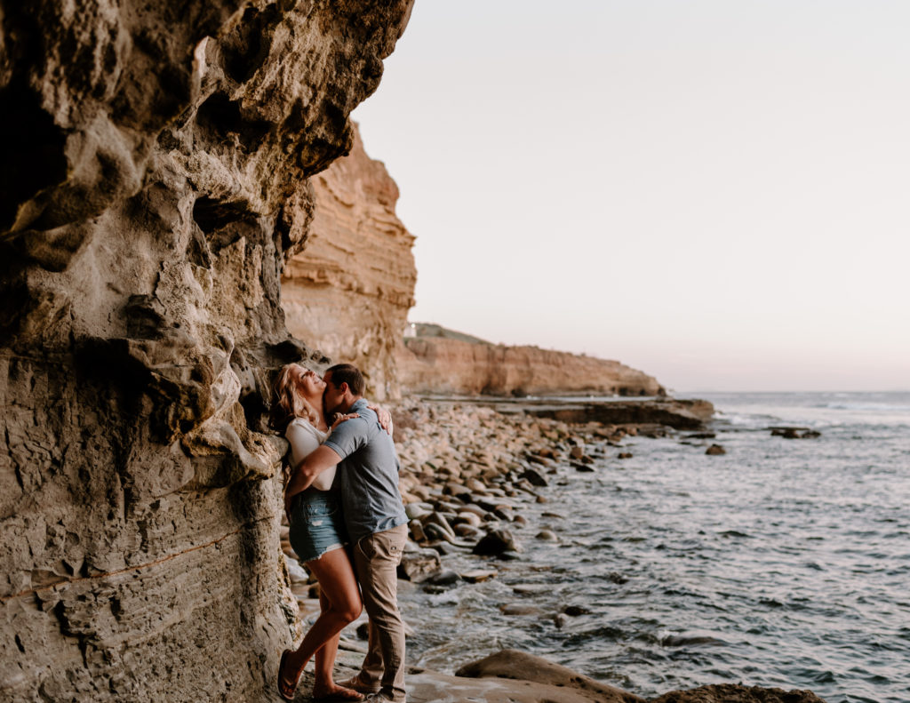 A photograph of a man and woman kissing near the ocean during their engagement session at Sunset Cliffs in San Diego, CA.