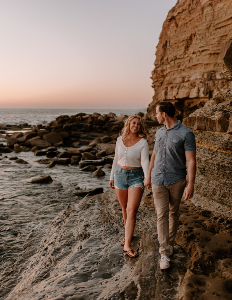 A photograph of a man and woman walking near the ocean during their engagement session at Sunset Cliffs in San Diego, CA.
