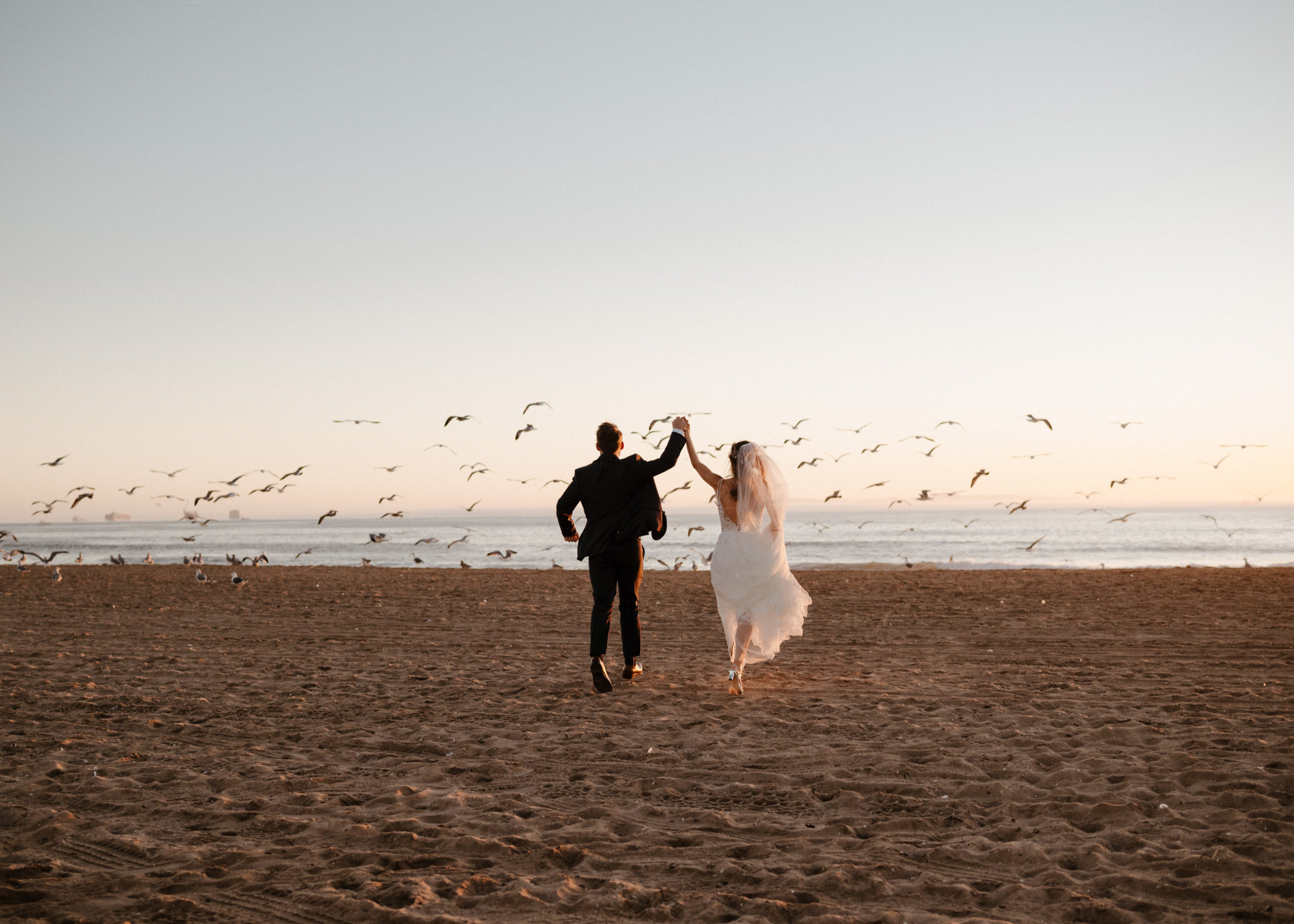 A bride and groom running through sand at their wedding on Coronado Beach in San Diego, CA.