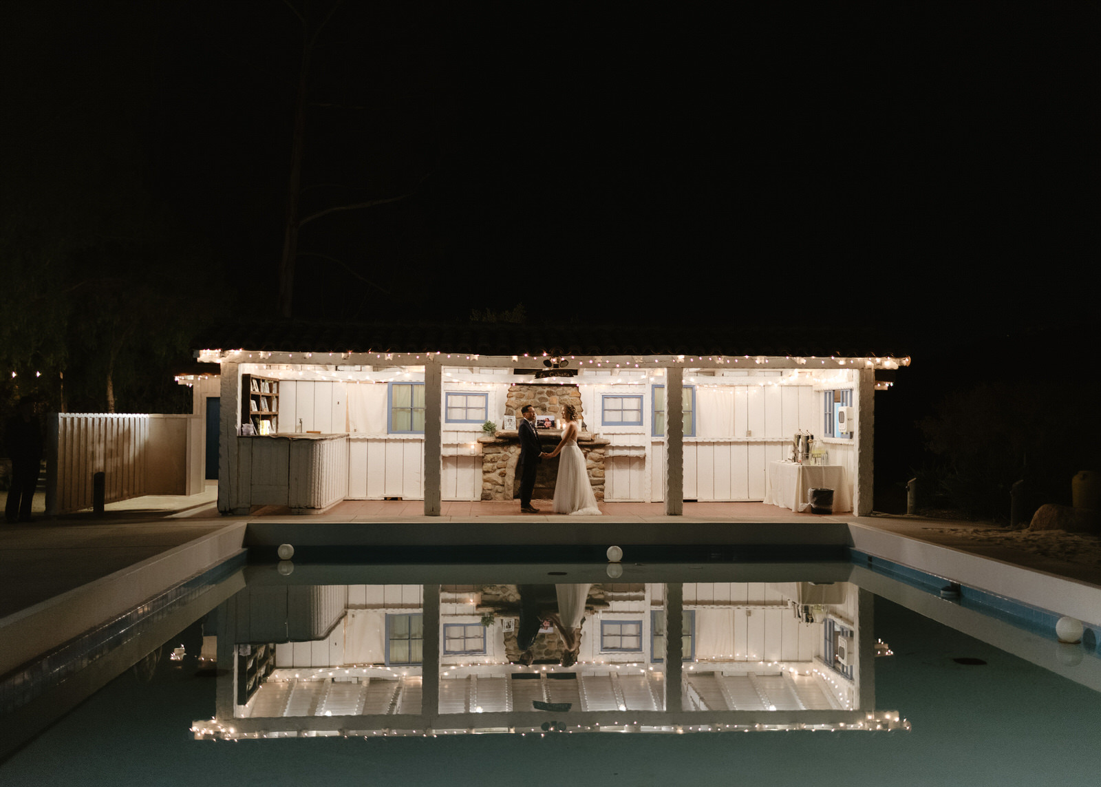 A bride and groom standing at night with their reflection in a pool at this Leo Carrillo Ranch wedding.